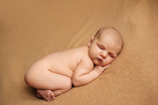 Newborn baby posed on a beige blanket with her hands under her cheeks at a newborn photo shoot