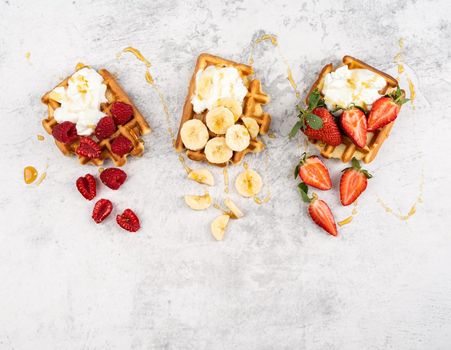 Traditional Belgian waffles with fresh fruit and cream on white marble background. Flat lay, top view, copy space.