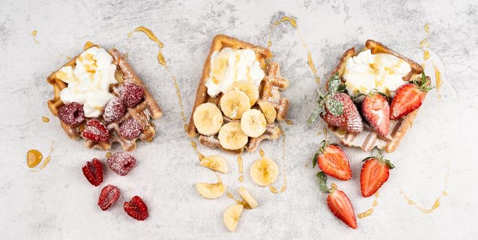 Traditional Belgian waffles with fresh fruit and cream on white marble background. Flat lay, top view, copy space.