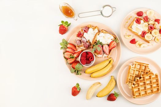 Homemade waffles with fruits and berries, cream and honey in a plate on white table. Flat lay, top view, copy space.