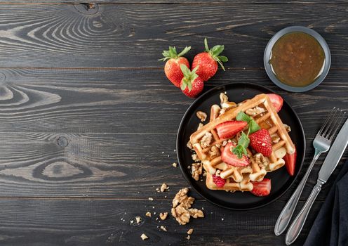 Flat lay of black plate with Belgian waffles with fresh stawberry on dark wooden background. Flat lay, top view copy space.