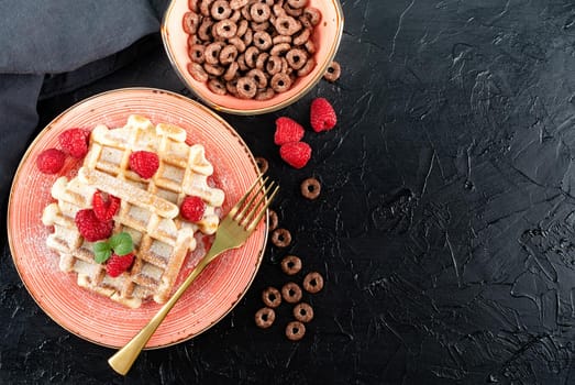 breakfast with waffles and a bowl of chocolate cereal on black backgrownd. Flat lay, top view, copy space.