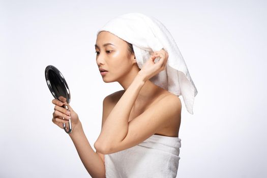 beautiful woman of asian appearance looks in the mirror with a towel on her head for spa treatments. High quality photo