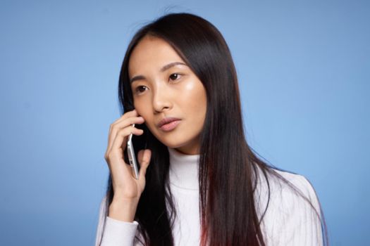 Asian woman talking on a cell phone on a blue background. High quality photo