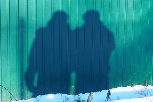 Two men reflected against the backdrop of a fence in sunny winter weather. High quality photo