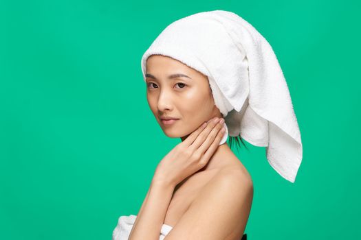 woman of asian appearance naked shoulders towel on head green background studio. High quality photo