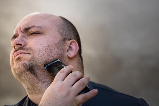 Male shaving or trimming his beard using a hair clipper or electric razor