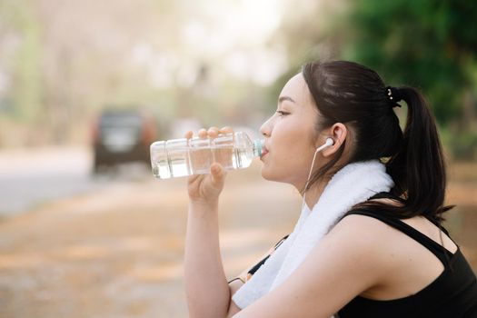 Young woman athlete takes a break, drinking water, out on a run on a hot day