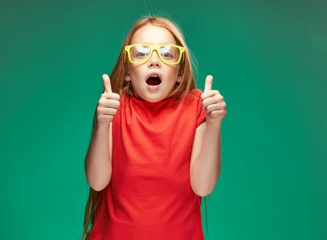 emotional red-haired girl in yellow glasses red t-shirt emotions studio green background. High quality photo