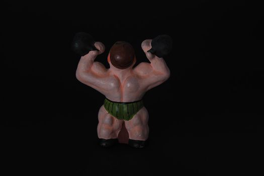 Athlete. Figures made of ceramics, plaster and clay. The man with the weights. Close-up. Black background.