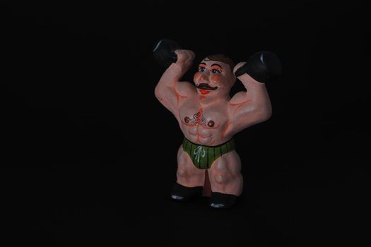 Athlete. Figures made of ceramics, plaster and clay. The man with the weights. Close-up. Black background.