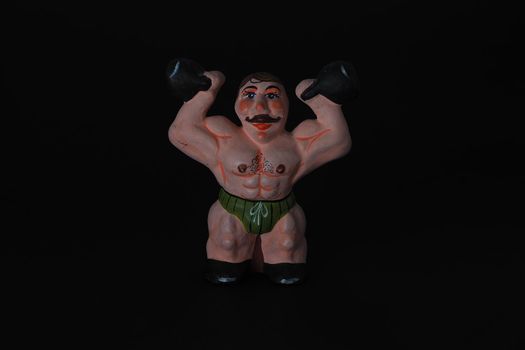 Athlete. Figures made of ceramics, plaster and clay. The man with the weights. Close-up. Black background.