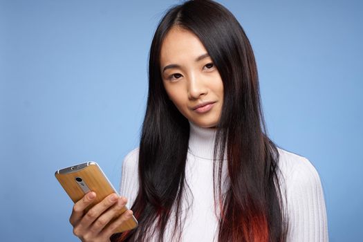 woman of asian appearance holding phone in hands internet communication technology blue background. High quality photo