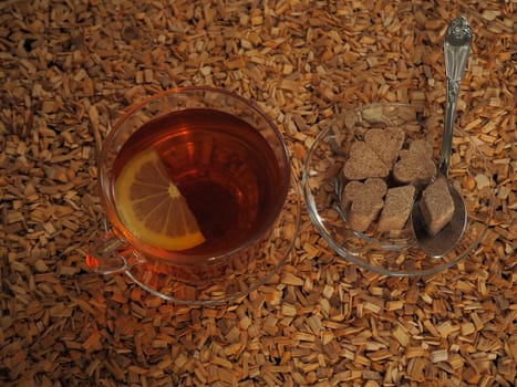 Black tea with lemon in a transparent cup on a wooden tray.