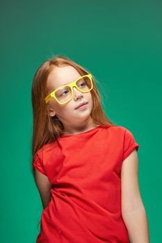 redhead girl with yellow glasses gesturing with her hands childhood learning Green background. High quality photo