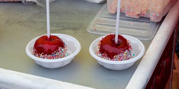 A red caramelized apple on a stick, covered in hard red sugar, standing in a plastic plate to serve as a festive treat. The concept of Easter, Maslenitsa,Valentine's Day.