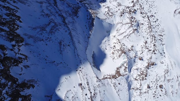 A huge wall of ice. Bogdanovich Glacier in the mountains of Almaty. The wind blows the snow away from the high frozen wave. Unusual shape and color of the ice. Moraine lake in winter in the mountains