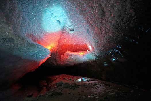 In an ice cave with colored lighting from lanterns. Snow and ice of interesting shapes grow on the walls of the cave. Stalactites hang. The huge ice walls shimmer with light. Macro photography. Almaty