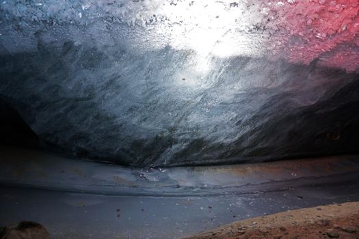 In an ice cave with colored lighting from lanterns. Snow and ice of interesting shapes grow on the walls of the cave. Stalactites hang. The huge ice walls shimmer with light. Macro photography. Almaty