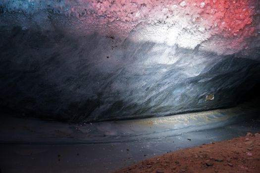 In an ice cave with colored lighting from lanterns. Snow and ice of interesting shapes grow on the walls of the cave. Stalactites hang. The huge ice walls shimmer with light. Macro photography. Almaty