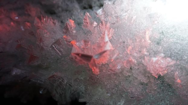 In an ice cave with colored lighting from lanterns. Snow and ice of interesting shapes grow on the walls of the cave. Stalactites hang. The huge ice walls shimmer with light. Macro photography. Almaty