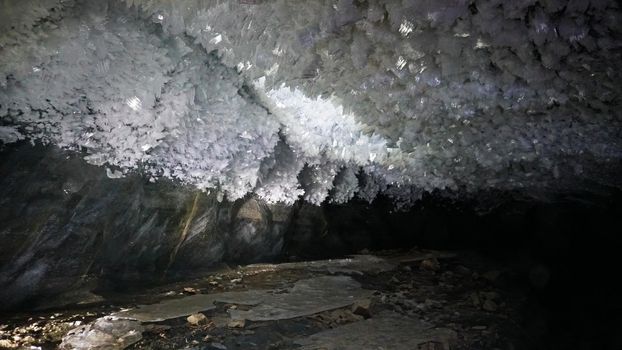 In an ice cave with colored lighting from lanterns. Snow and ice of interesting shapes grow on the walls of the cave. Stalactites hang. The huge ice walls shimmer with light. Macro photography. Almaty