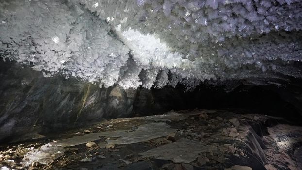 In an ice cave with colored lighting from lanterns. Snow and ice of interesting shapes grow on the walls of the cave. Stalactites hang. The huge ice walls shimmer with light. Macro photography. Almaty