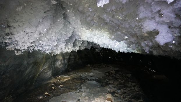 In an ice cave with colored lighting from lanterns. Snow and ice of interesting shapes grow on the walls of the cave. Stalactites hang. The huge ice walls shimmer with light. Macro photography. Almaty