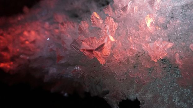 Macro photography of ice growths in a cave. Snow and ice of interesting shapes grow on the walls of the cave. Stalactites hang. Huge ice walls shimmer from the light of the lantern. Almaty, Kazakhstan