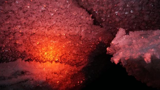 Macro photography of ice growths in a cave. Snow and ice of interesting shapes grow on the walls of the cave. Stalactites hang. Huge ice walls shimmer from the light of the lantern. Almaty, Kazakhstan