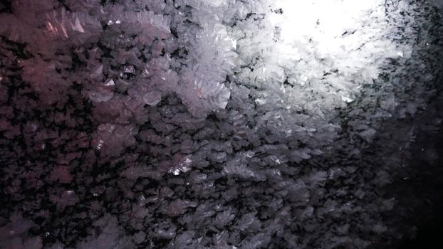 Macro photography of ice growths in a cave. Snow and ice of interesting shapes grow on the walls of the cave. Stalactites hang. Huge ice walls shimmer from the light of the lantern. Almaty, Kazakhstan