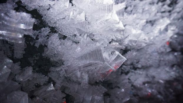 Macro photography of ice growths in a cave. Snow and ice of interesting shapes grow on the walls of the cave. Stalactites hang. Huge ice walls shimmer from the light of the lantern. Almaty, Kazakhstan