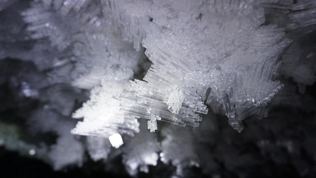 Macro photography of ice growths in a cave. Snow and ice of interesting shapes grow on the walls of the cave. Stalactites hang. Huge ice walls shimmer from the light of the lantern. Almaty, Kazakhstan