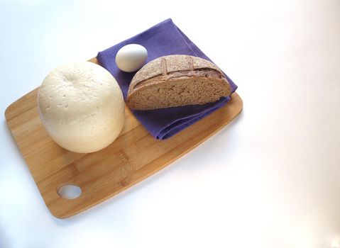 Round head of cheese with cut rustic fresh bread on a wooden tray.