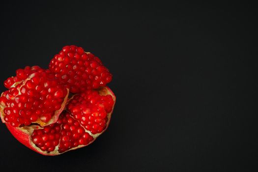 The fruit of a ripe pomegranate. Red fruit with juicy grains. Isolated on a black background. Close-up.