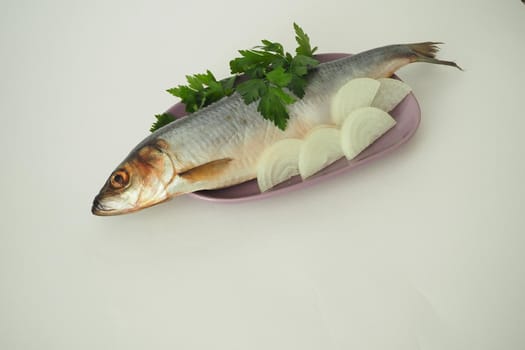 Fish. It's a whole herring. Undivided herring with onions and parsley. Close-up, white background.