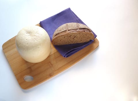 Round head of cheese with cut rustic fresh bread on a wooden tray.