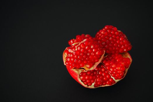 The fruit of a ripe pomegranate. Red fruit with juicy grains. Isolated on a black background. Close-up.