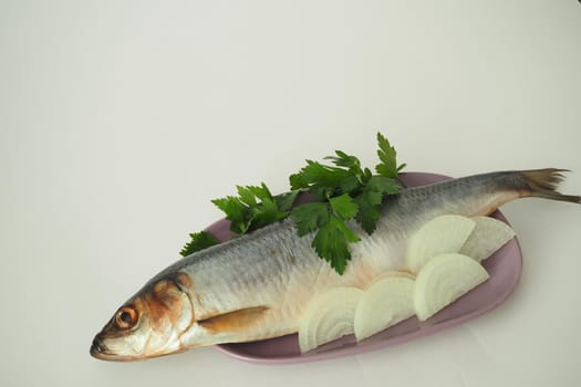 Fish. It's a whole herring. Undivided herring with onions and parsley. Close-up, white background.