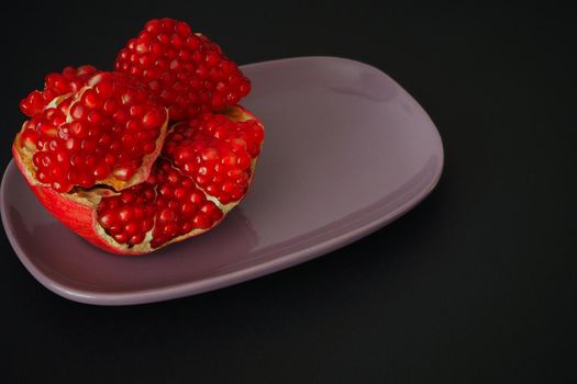 The fruit of a ripe pomegranate. Red fruit with juicy grains. Isolated on a black background. Close-up.