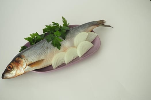 Fish. It's a whole herring. Undivided herring with onions and parsley. Close-up, white background.