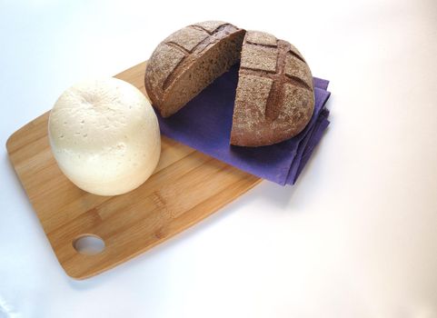 Round head of cheese with cut rustic fresh bread on a wooden tray.