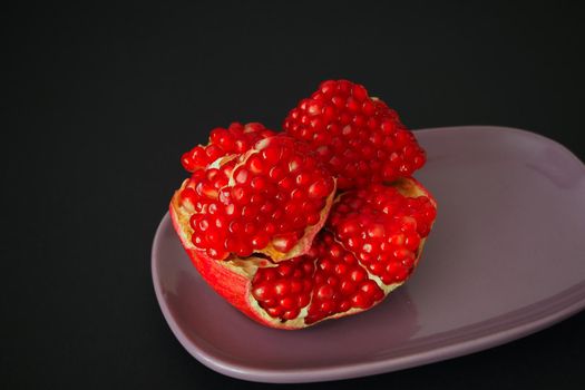 The fruit of a ripe pomegranate. Red fruit with juicy grains. Isolated on a black background. Close-up.