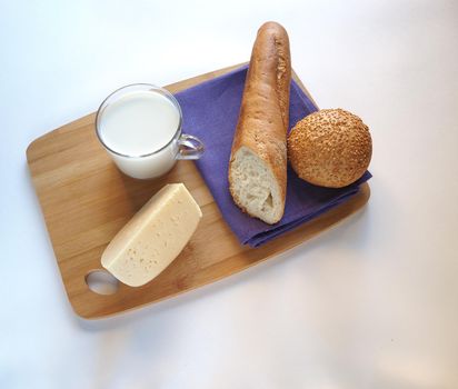 A piece of cheese with baguette and a glass of milk on a wooden tray.