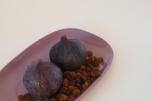 Exotic fruits and berries. Fig and raisins on a purple platter. White background. Close-up. High quality photo