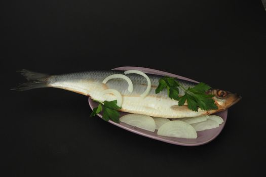 Herring whole, undivided with onion and parsley, close-up. Fish on a platter. Black background.