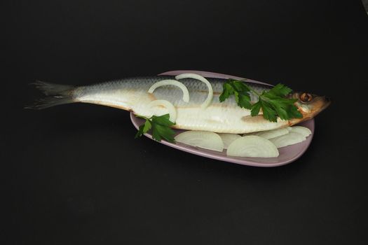 Herring whole, undivided with onion and parsley, close-up. Fish on a platter. Black background.