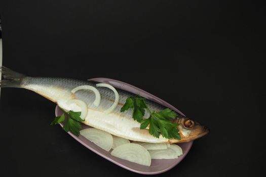 Herring whole, undivided with onion and parsley, close-up. Fish on a platter. Black background.