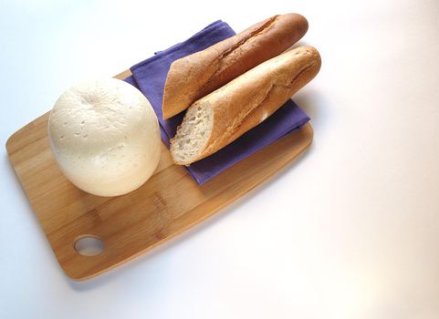 A large piece of cheese on a wooden tray with fresh bread. A high-quality photo. Close-up