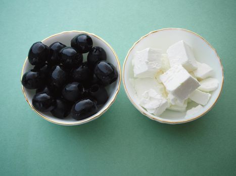 Ingredients for Greek salad feta cheese and black olives in a salad bowl.